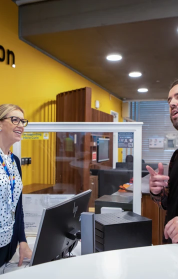 Receptionist assisting a student at the Glasgow Kelvin College Springburn Campus reception desk, both smiling and engaged in conversation. Receptionist assisting a student at the Glasgow Kelvin College Springburn Campus reception desk, both smiling and engaged in conversation.